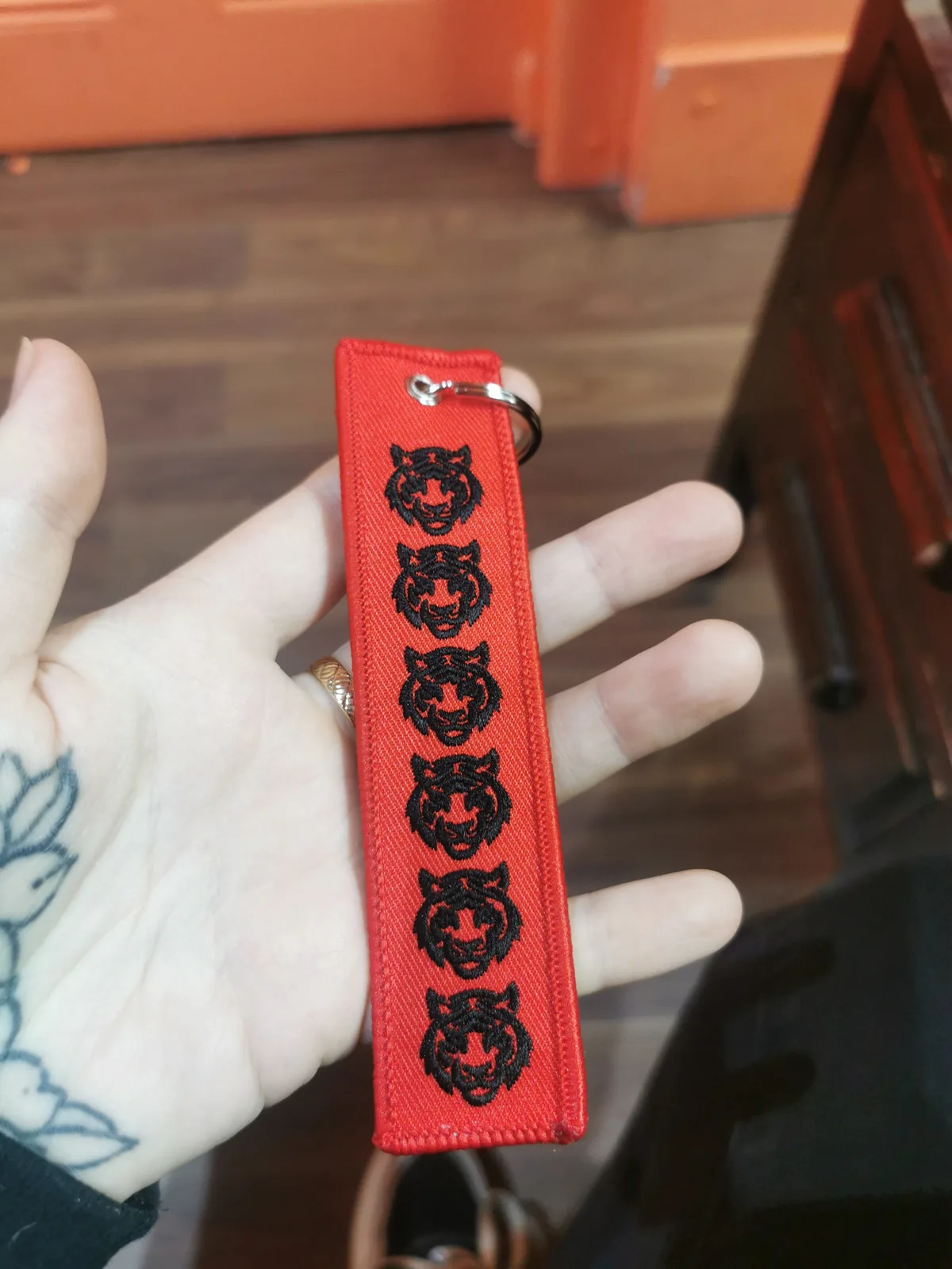 Red embroidered keychain tag with six tiger heads, held in a hand